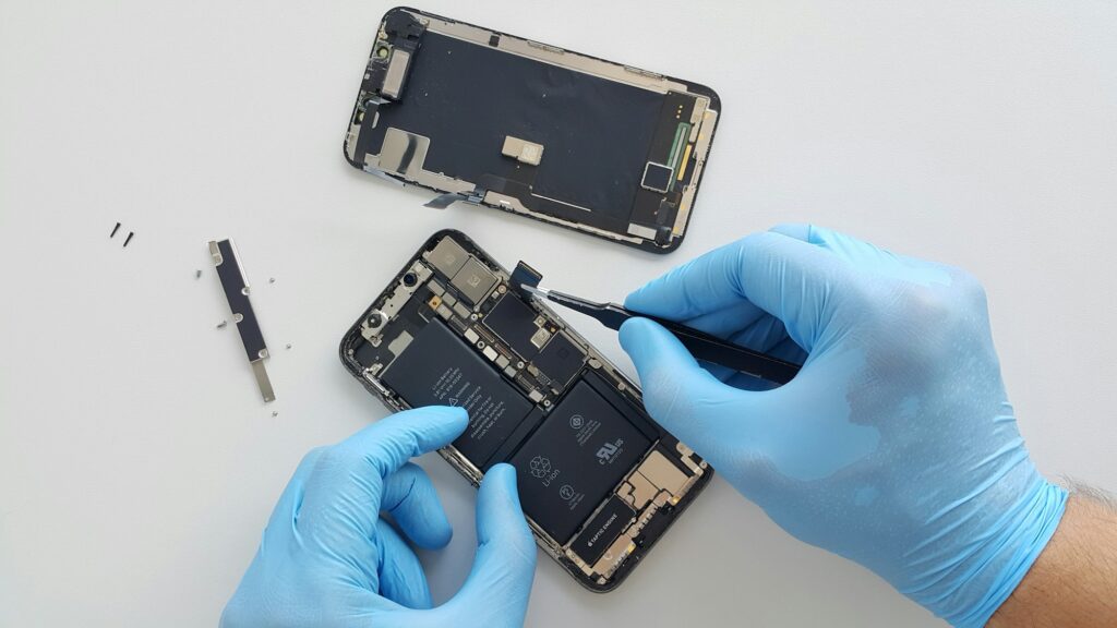Tecnico con guanti blu interviene sui componenti interni di uno smartphone