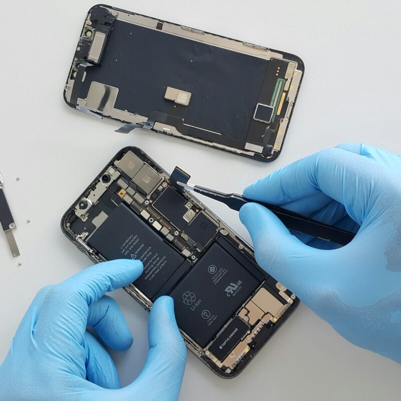 Tecnico con guanti blu interviene sui componenti interni di uno smartphone
